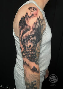 Tatouage en noir et gris d'un gorille dans la brune sur le bras d'une homme.