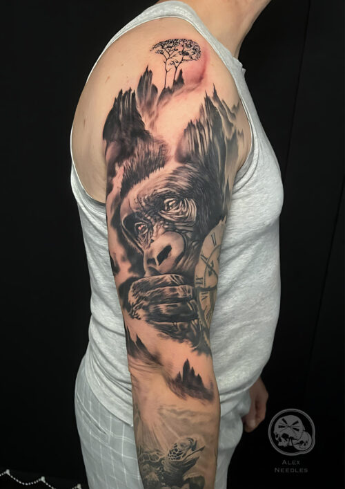 Tatouage en noir et gris d'un gorille dans la brune sur le bras d'une homme.