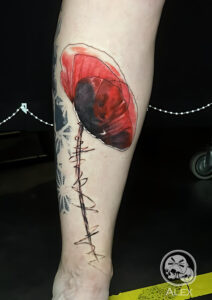 Tatouage représentant un coquelicot graphique en couleurs sur une jambe réalisé par Alex, The Needles Factory