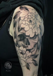Tatouage représentant un crane réaliste et deux pivoines en noir et gris sur un bras réalisé par Alex, The Needles Factory