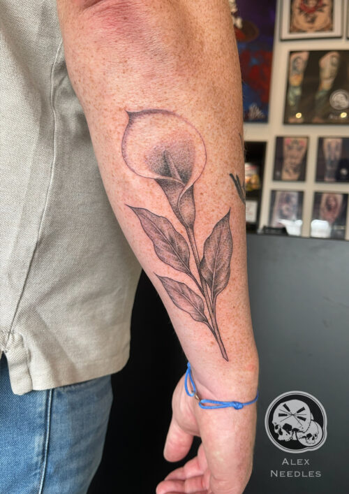 Tatouage d'une fleur Arum sur l'arrière d'un avant-bras en noir et gris réalisé par Alex, The Needles Factory