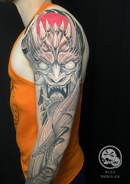 Tatouage d'un masque d'Oni en noir et gris avec un touche de rouge sur le haut du tatouage. Projet réalisé sur un bras complet par Alex, The Needles Factory