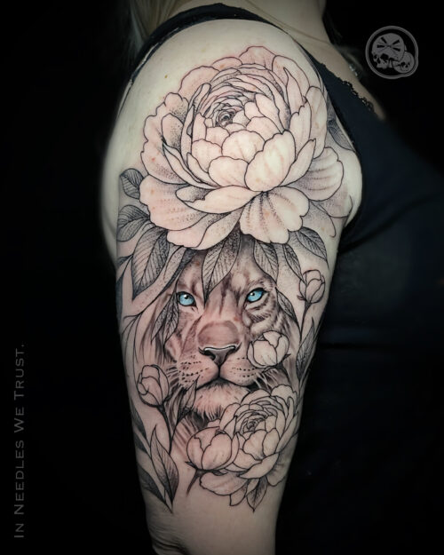 Tatouage lion réaliste aux yeux bleus entouré de pivoines, noir et gris (dotwork), réalisé à Boulogne-sur-Mer (62) chez The Needles Factory.
