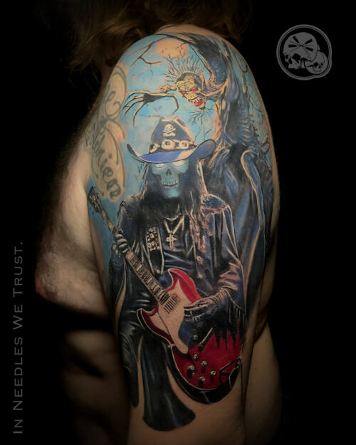 Tatouage réaliste couleur sur épaule : squelette guitariste et créature, réalisé à Boulogne-sur-Mer (The Needles Factory)