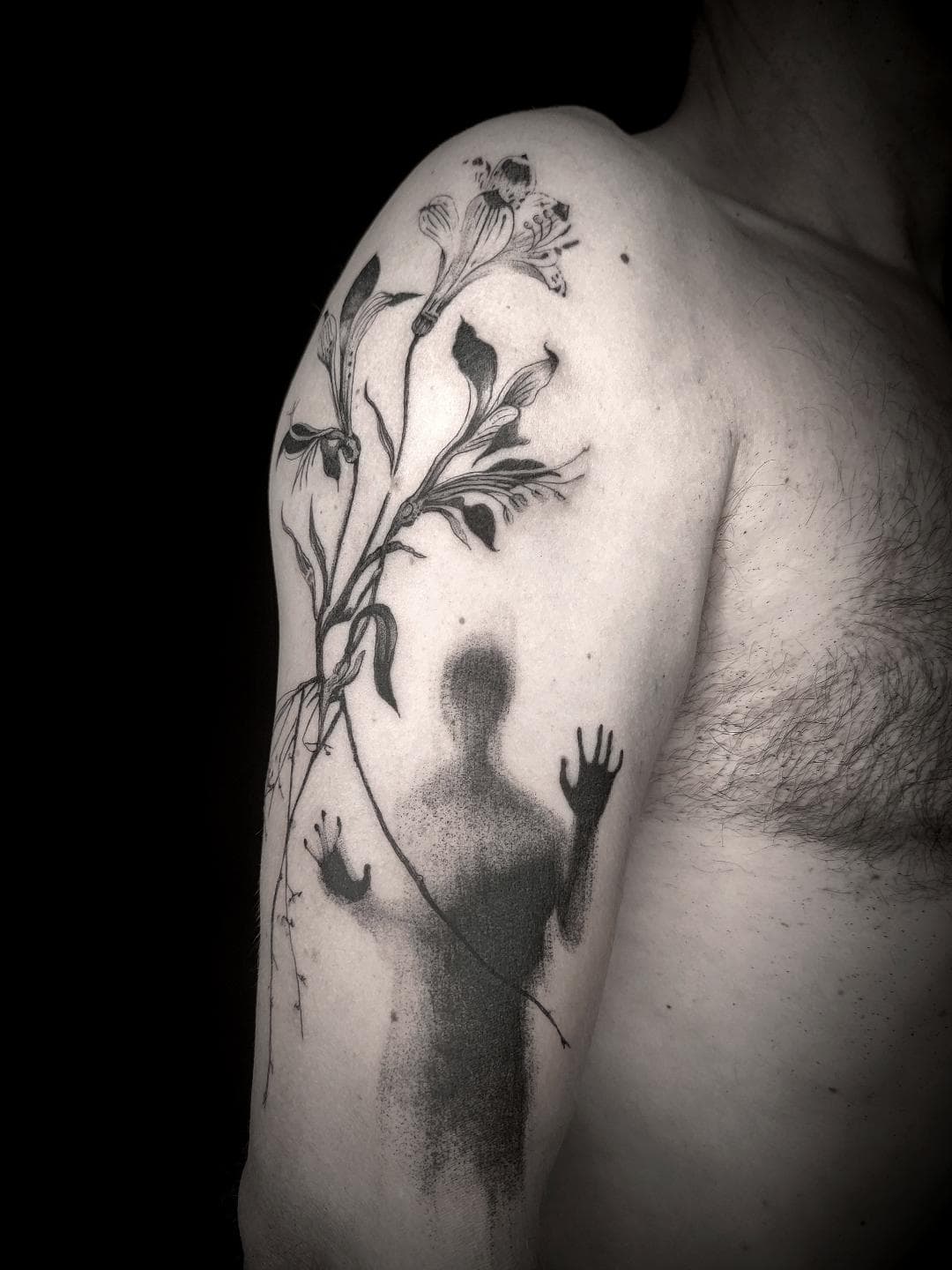 Tatouage noir d’une silhouette et de fleurs sur le bras